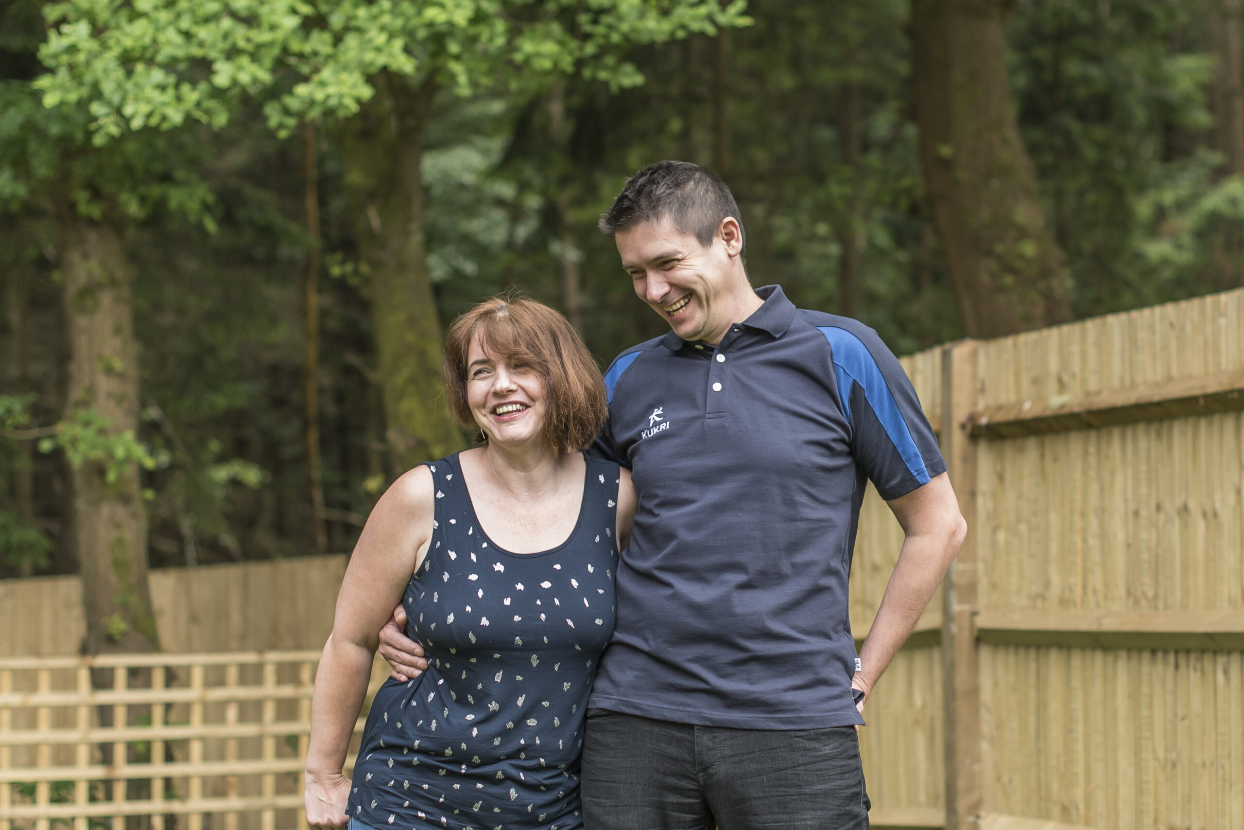 Anca and Lucian in the garden beside a wooden fence