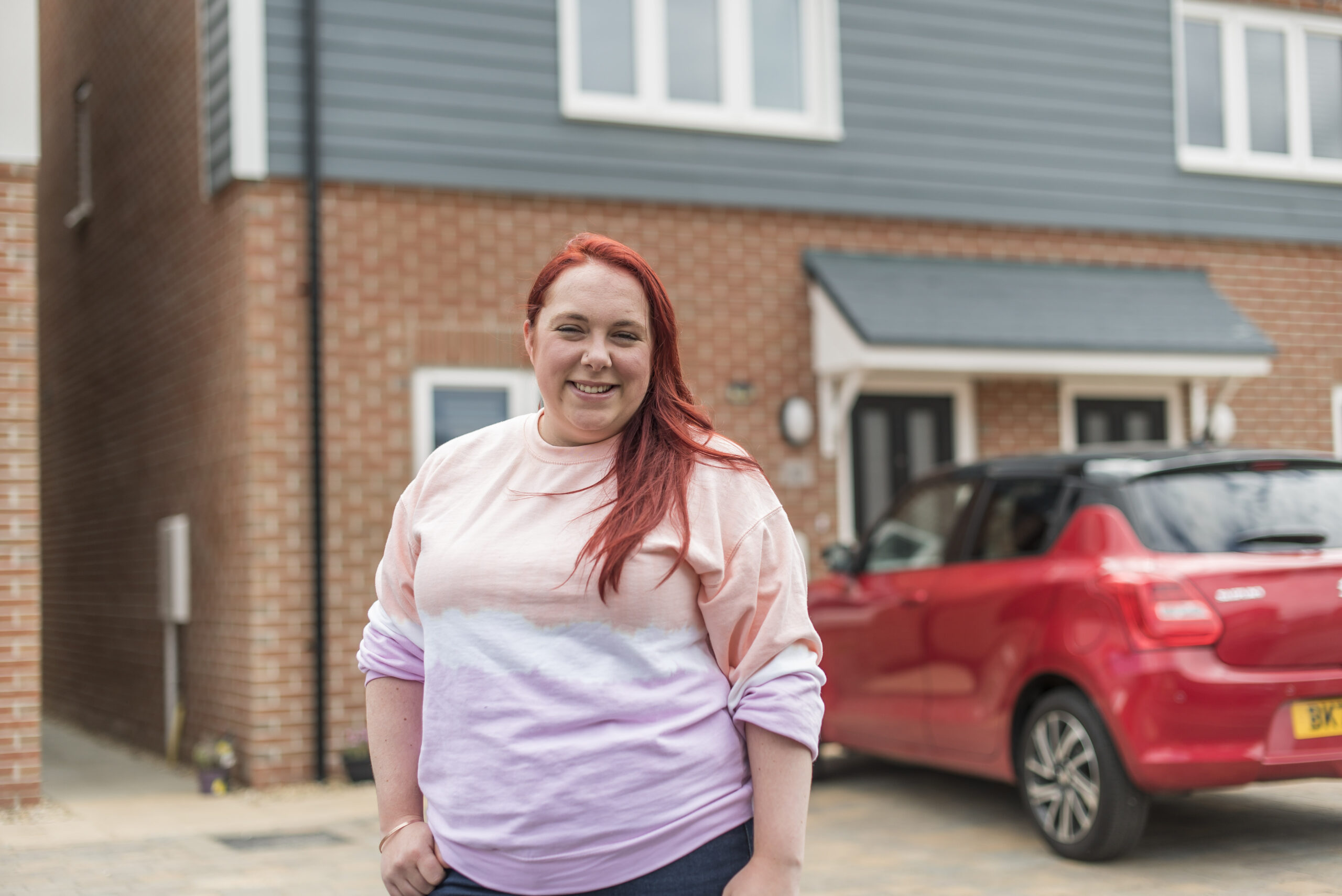 Zoe outside her home with a red car on the driveway