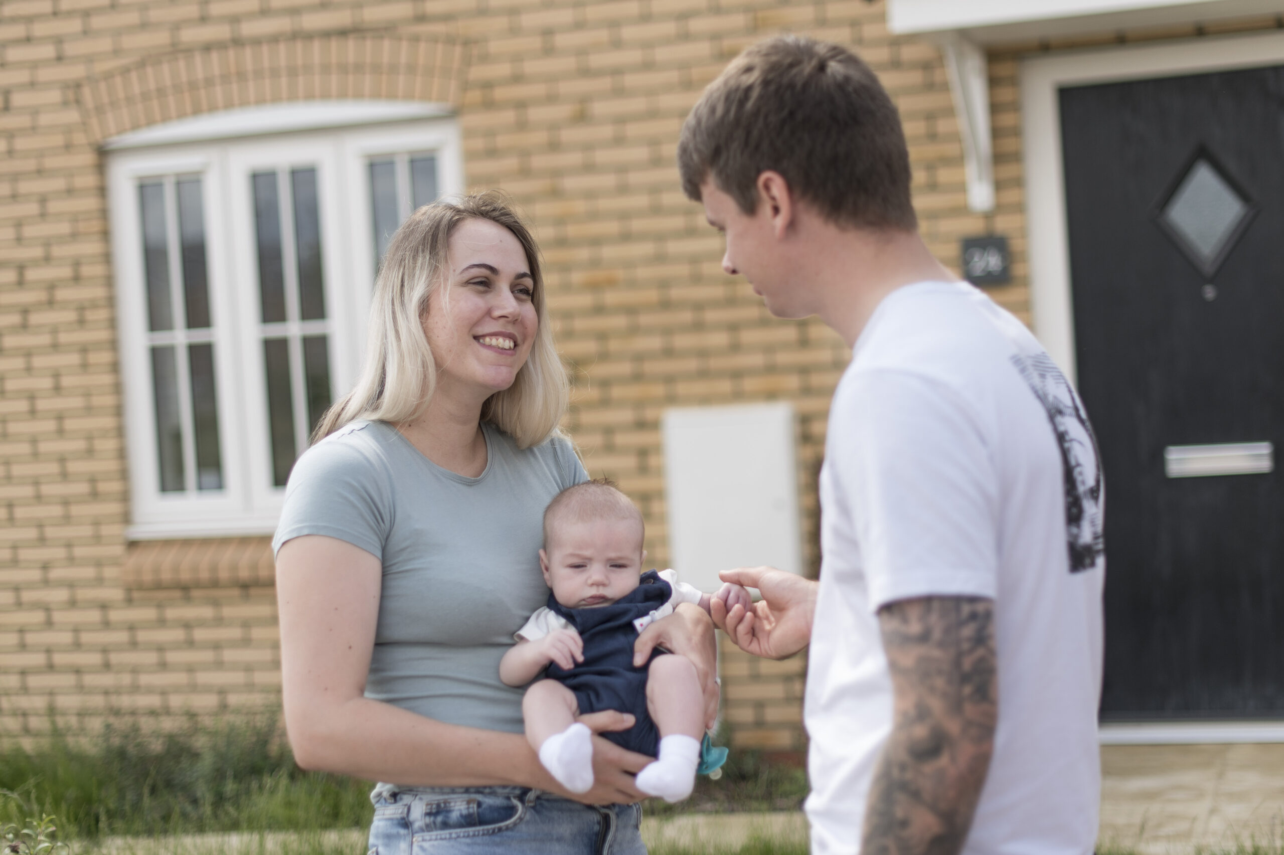 Vikki holding their baby with Mitch at the front door