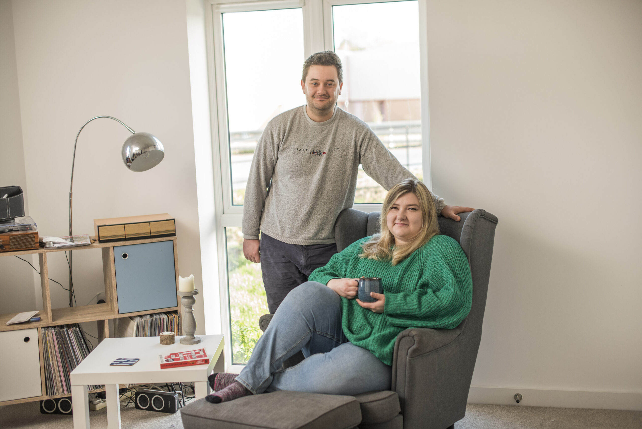 Maddison seated and Daniel standing in their living room