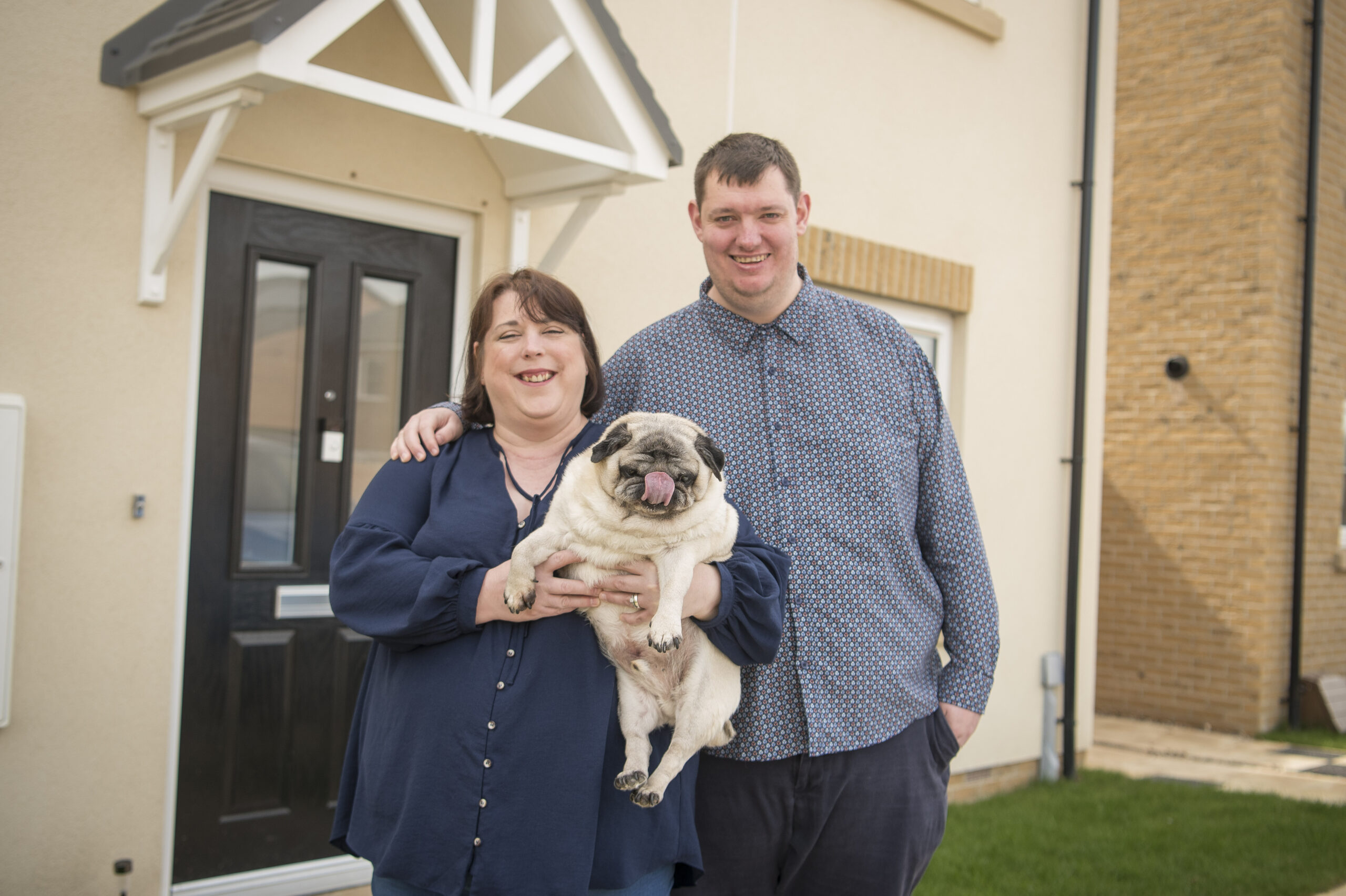 Dee and Lewis holding their pug outside their front door