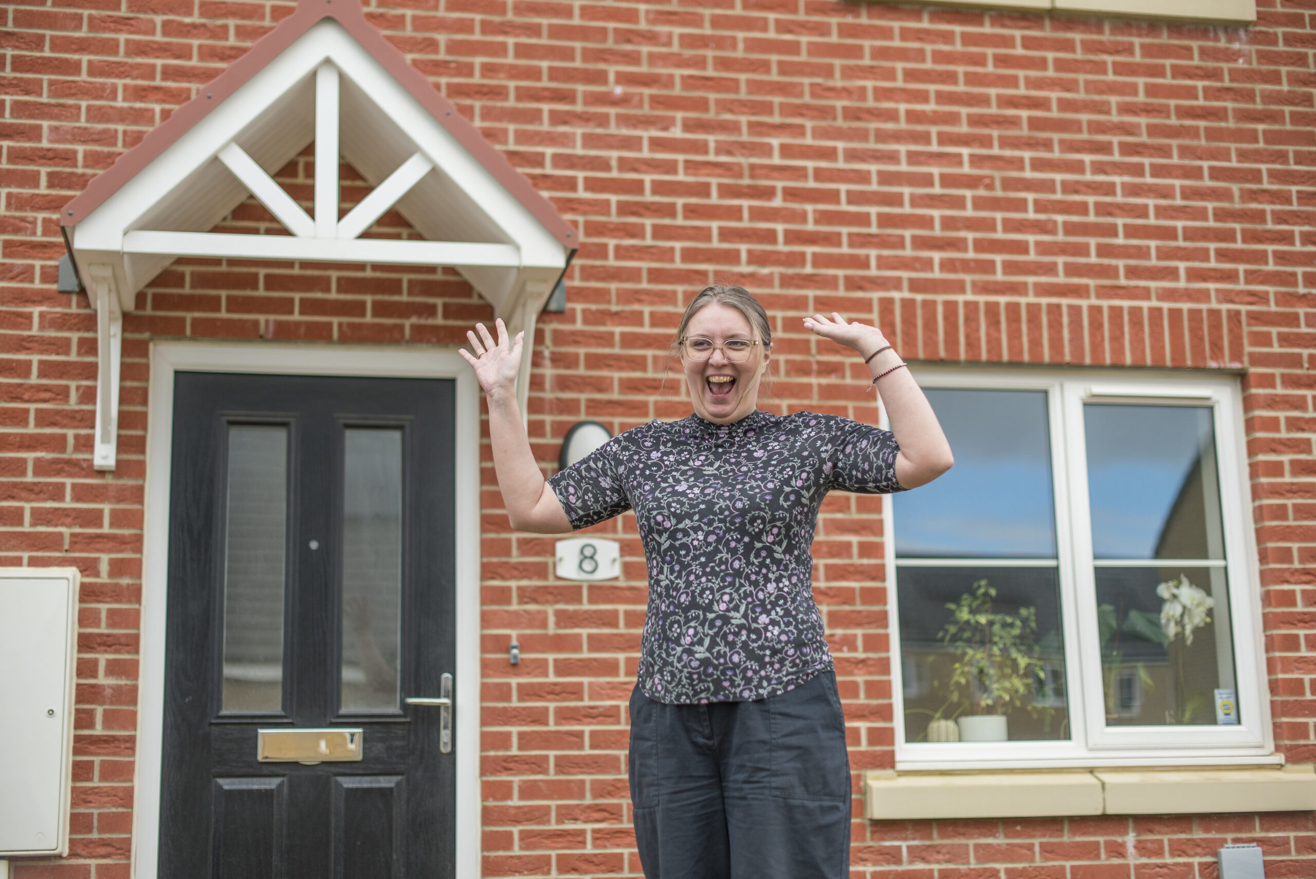 Katarzyna waving at the front door of her red-brick home