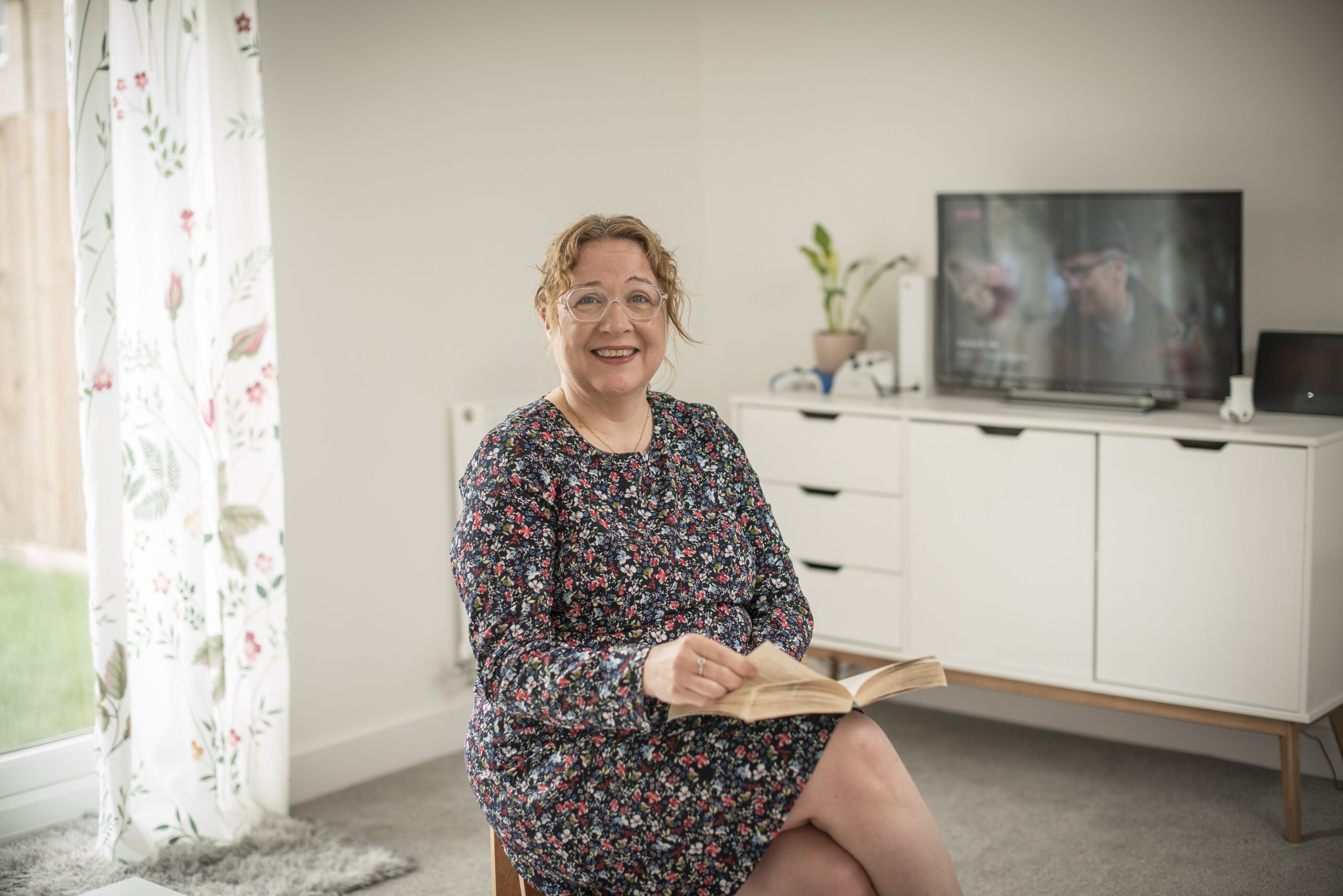 Katie reading a book beside a white sideboard