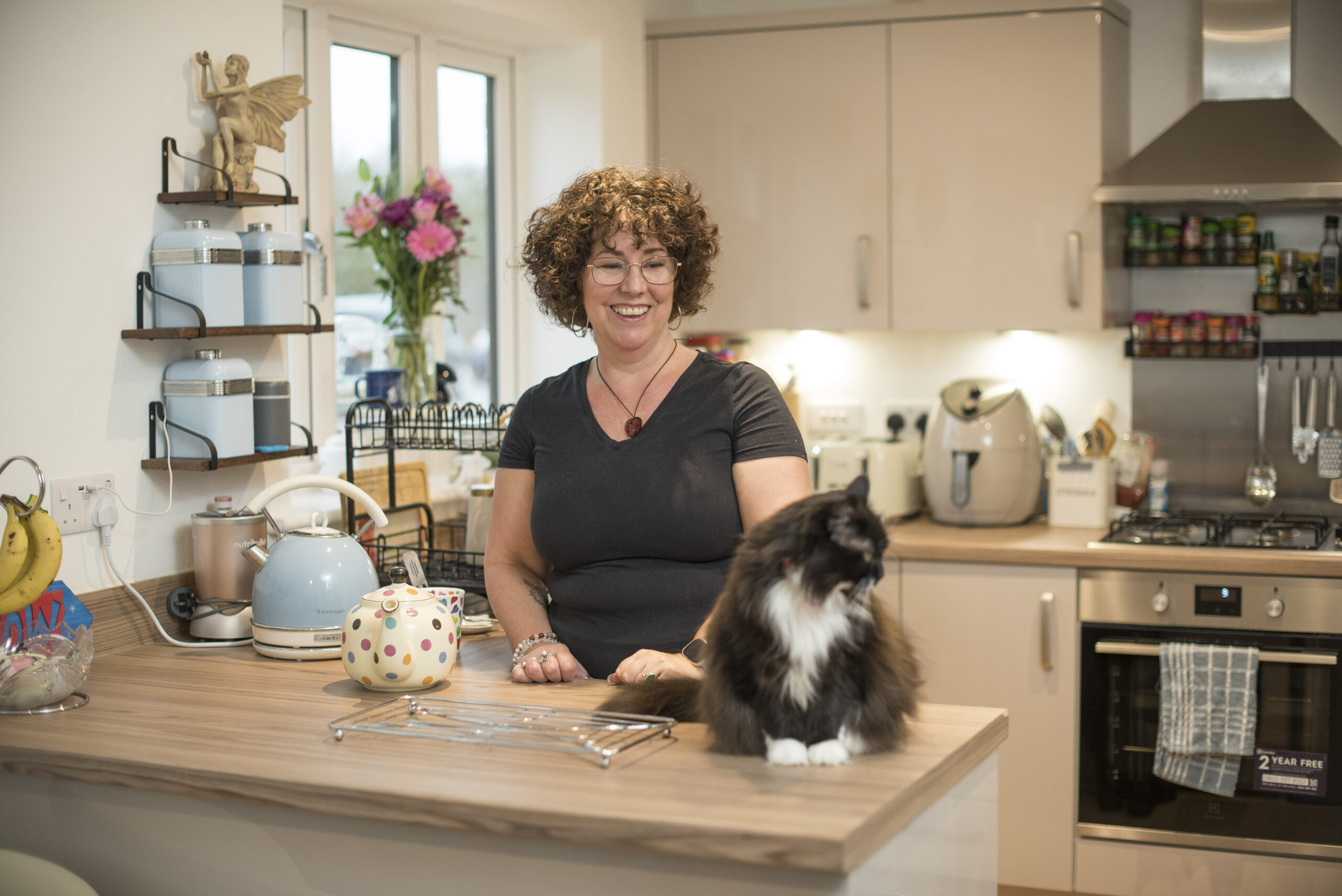 Lisa standing at the kitchen island of her home, with a black and white cat on the worktop